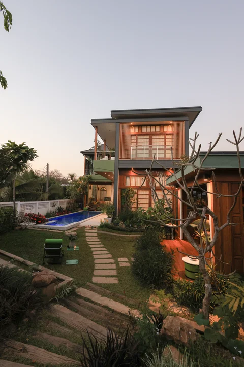 Villa exterior at dusk - two-storey facade with garden, stepping stone path, pool and frangipani tree