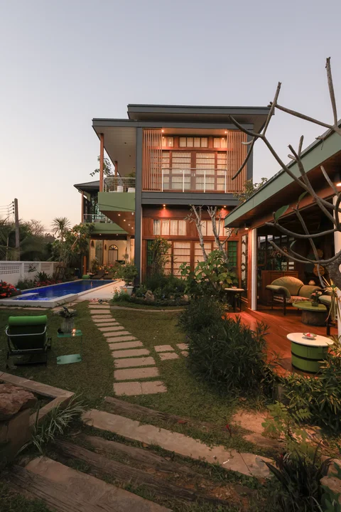 Villa exterior at dusk with the outdoor sala lit up and a frangipani tree in the foreground