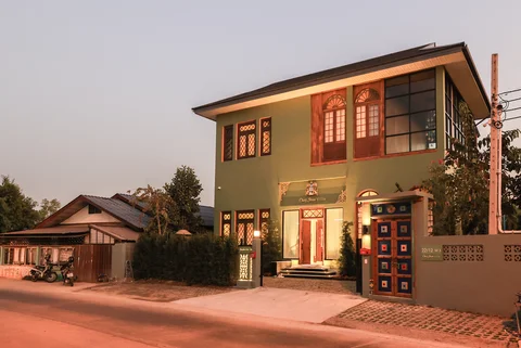 Villa exterior at dusk from the street - sage green facade, stained glass windows and decorative gate