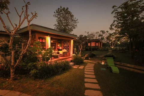 Garden at night with illuminated sala pavilion, stepping stone path and lime green pool loungers