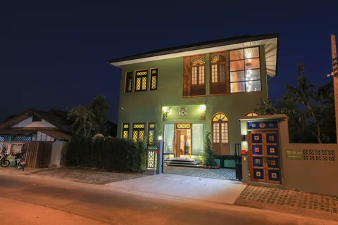 Villa front exterior at night with illuminated sage green facade and decorative mosaic gate