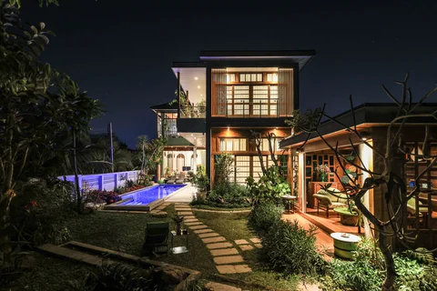 Villa exterior at night from garden with glowing blue pool and lit two-storey facade