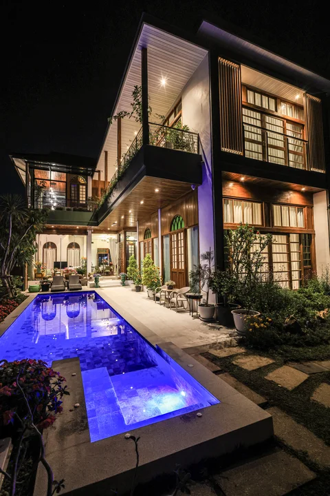 Striking night shot of the blue-lit pool with the villa's two-storey facade glowing behind it