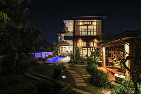 Villa at night from the garden showing blue pool glow and the lit sala pavilion