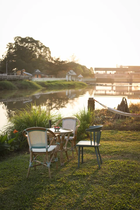 Riverside garden with wicker chairs, small table and hammock at golden sunset over the water