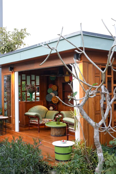 Garden sala pavilion with green rattan sofas, wooden barrel table, decorative plates and frangipani tree