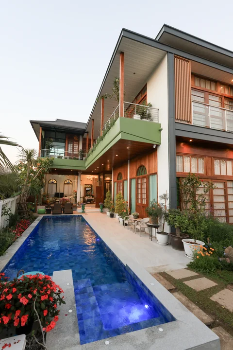 Villa exterior at dusk with blue pool in foreground, two-storey facade and red bougainvillea