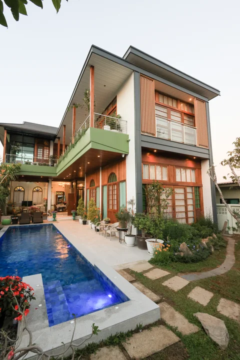 Villa exterior at dusk from a wider angle showing pool, two-storey facade and tropical garden