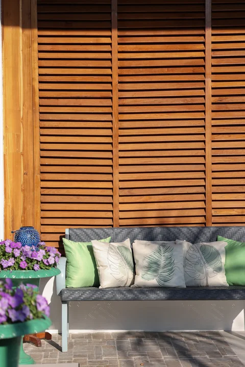 Outdoor sofa with tropical leaf-print cushions against a warm wooden louvred wall