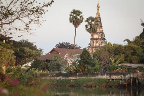 Chiang Mai Buddhist chedi and palm trees reflected in the river, viewed from the villa garden