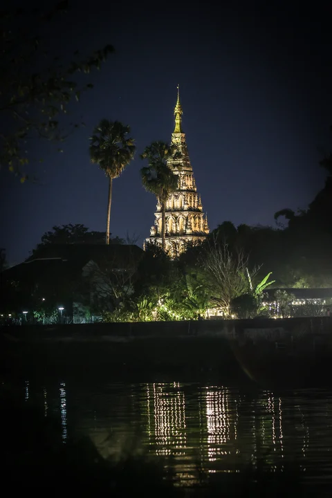 The Chiang Mai Buddhist chedi illuminated at night, beautifully reflected in the river below